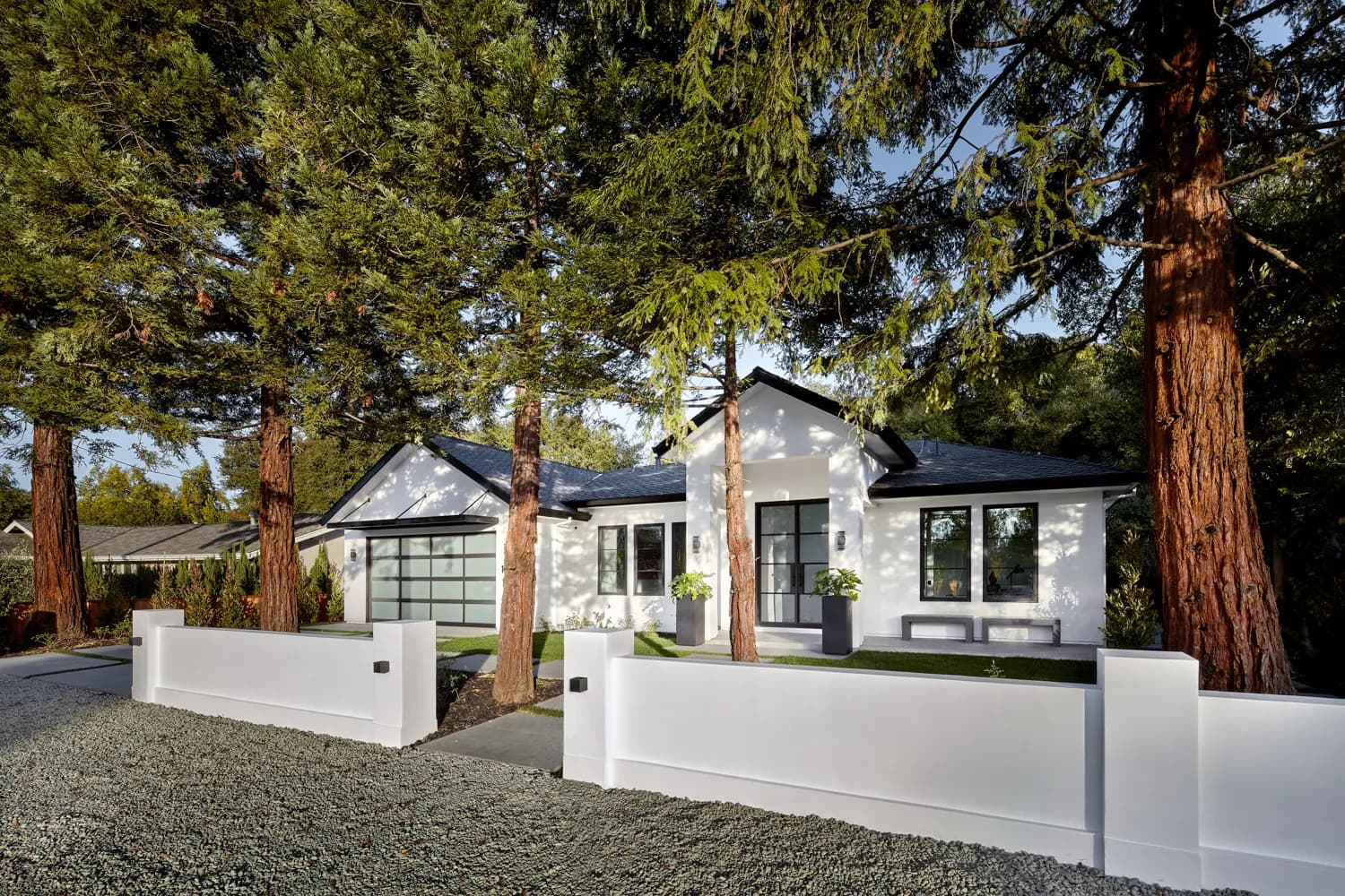 Single-story custom home in Los Altos among redwoods, with white stucco walls, a dark hipped roof and a frosted glass garage door